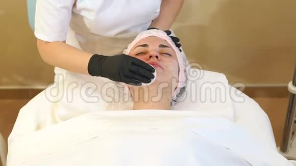 美容师的双手用白餐巾纸擦拭温泉沙龙里的姑娘们的脸视频的预览图