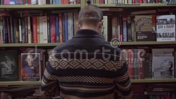 一个年轻人在书店里选择一本书然后转过身来面对相机视频的预览图
