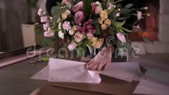 专业女性花艺师花艺师包花粉红色玫瑰在礼品纸在车间家庭工作室花卉学视频的预览图