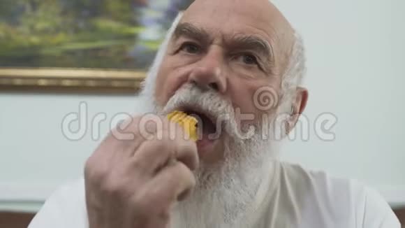 家中坐在皮沙发上吃薯片的老胡子老头的特写肖像视频的预览图