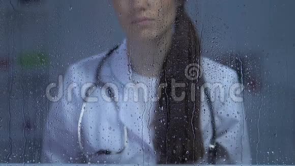 病人死亡抑郁后不高兴的女医生在雨窗里看着视频的预览图