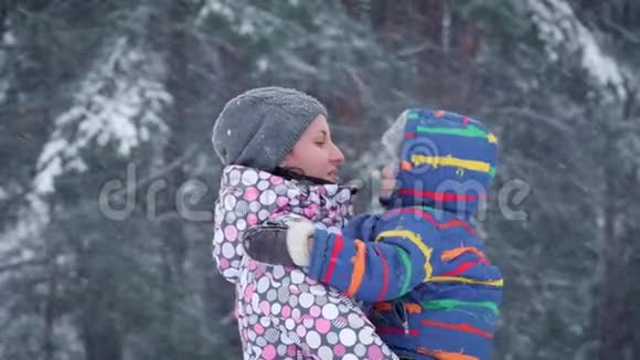 一位快乐的母亲在冬天森林的背景下亲吻她的孩子两个人在一个下雪的冬天视频的预览图