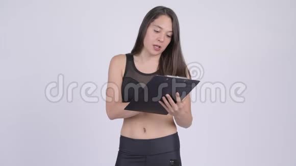 年轻快乐的女人一边说话一边在剪贴板上看书准备健身房视频的预览图