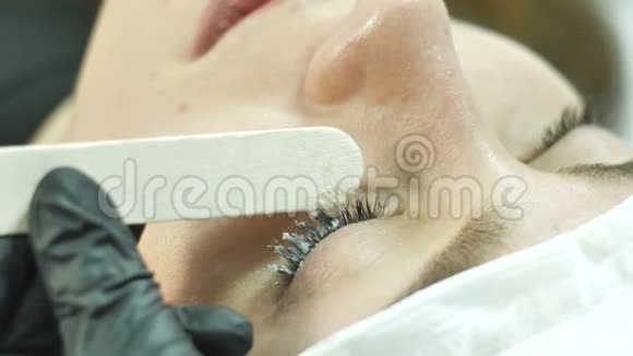 美容院老板在顾客的睫毛上涂上一种物质用海绵和海绵把睫毛复原视频的预览图