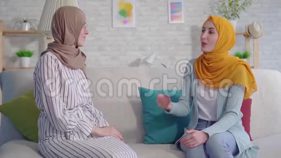 在客厅里两位戴着头巾面带微笑失聪的年轻穆斯林妇女用手语交谈视频的预览图