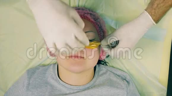 一位戴着手套的男性美容师的手将胶原蛋白垫放在女性脸上的眼睛下面视频的预览图