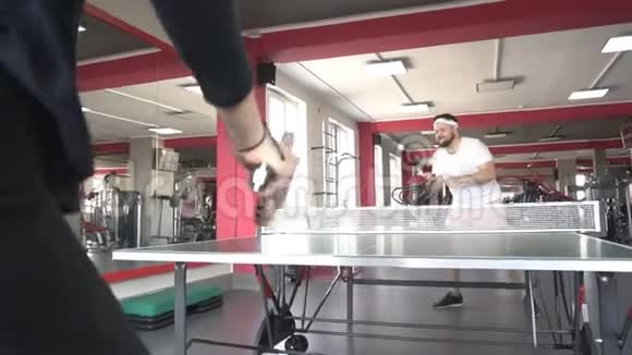 白种人朋友和漂亮的漂亮女孩在现代健身房打乒乓球慢动作生活方式比赛视频的预览图