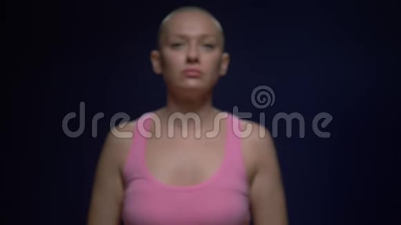 那个在癌症中幸存下来的秃头女人在黑暗的背景下小心翼翼地手里拿着一条粉红色的丝带重点视频的预览图