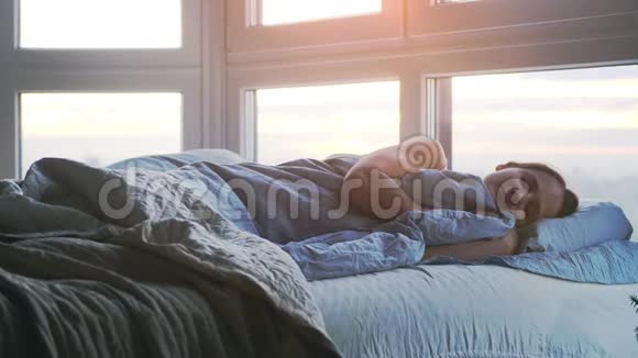 美丽浪漫的黑发女人躺在床上早上在房间里藏着毯子打哈欠慢动作视频的预览图