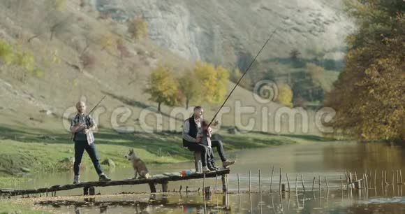 两个男人和一个小男孩正准备从湖里钓鱼一只哈士奇小狗钓鱼的地方真不错视频的预览图