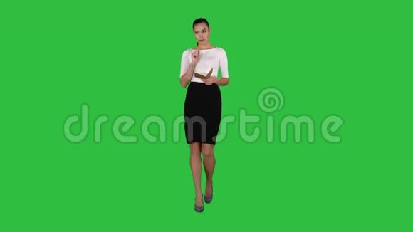 年轻女性在绿色屏幕上行走时做笔记色度键视频的预览图