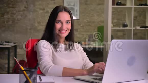在办公室工作的女人在笔记本电脑前对着镜头摆姿势微笑视频的预览图