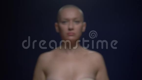 那个在癌症中幸存下来的秃头女人在黑暗的背景下小心翼翼地手里拿着一条粉红色的丝带关注重点视频的预览图
