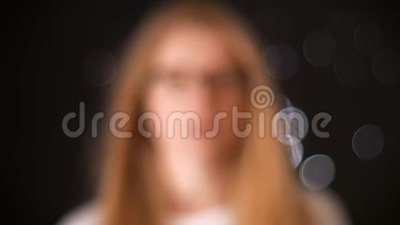 一副漂亮的金发眼镜白种人女人站在室内黑色背景下密切注视镜头视频的预览图
