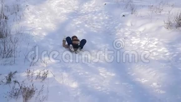 年轻的女孩骑在冬天的公园里坐在一座高高的雪山上的雪橇上圣诞节假期视频的预览图