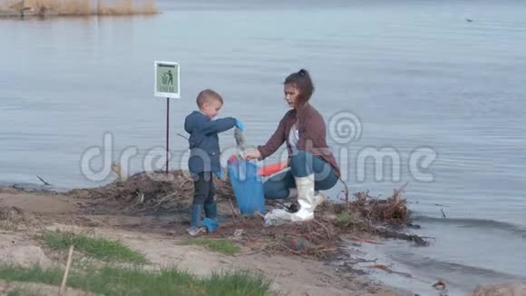 塑料污染问题女孩带着男孩志愿者从河边的水附近的塑料垃圾中清理肮脏的海岸视频的预览图