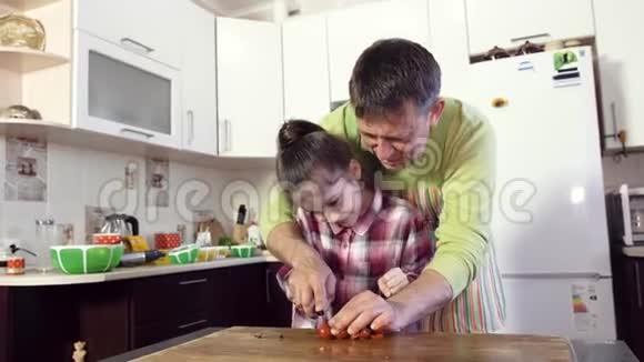 厨房里的一位父亲教他的女儿用刀切蔬菜视频的预览图