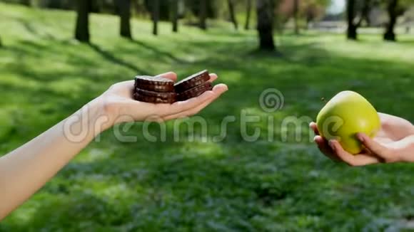 手选择吃什么绿色苹果或巧克力烘焙背景中有公园天气晴朗的概念视频的预览图