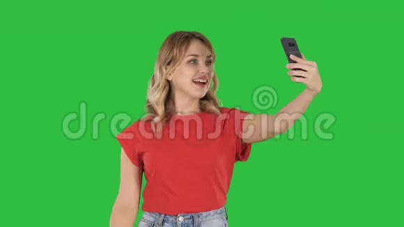 开朗的女性博主一边录制视频到现代电话的前置摄像头上一边走在绿色的屏幕上色度键视频的预览图