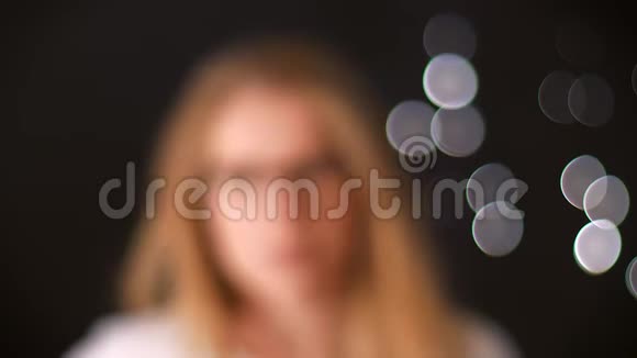 拍摄眼镜的女孩从模糊的黑色背景走向相机专注快乐的华丽面孔视频的预览图