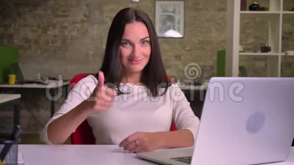 办公室里的女商人在手提电脑前看着相机把手指举起来显示类似的东西视频的预览图