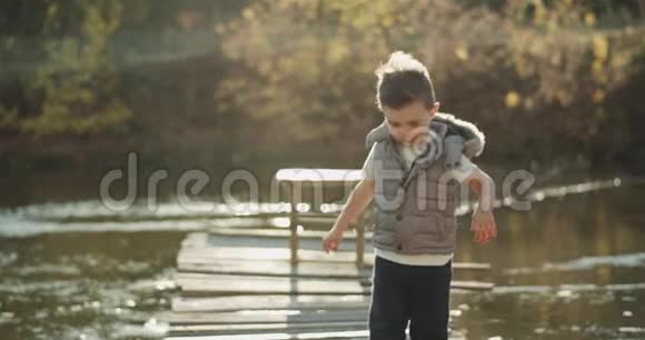 一个非常棒的小男孩站在湖边的桥顶上直视着镜头视频的预览图