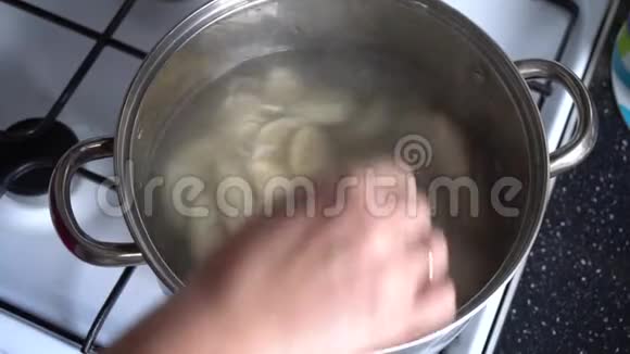 厨房里的一个女人在煤气灶旁边的一个锅里煮饺子视频的预览图