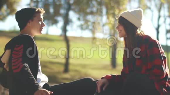 坐在公园里阳光下的嬉皮士男人和女孩交流青少年在户外放松滑板女孩视频的预览图