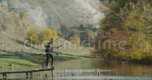 阳光明媚的一天一个男人从湖边钓鱼站在桥上视频的预览图