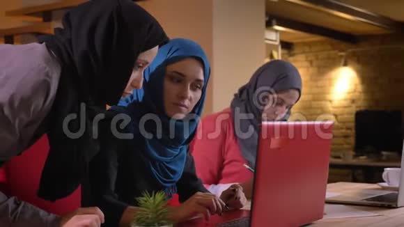 两名年轻的穆斯林女性员工用笔记本电脑讨论这个话题的特写照片三个伊斯兰团体视频的预览图