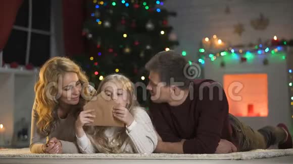 女孩带着父母把圣诞老人的信封粘在圣诞树下微笑着对着镜头视频的预览图