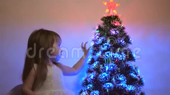小孩子在儿童房的圣诞树旁玩耍女儿在圣诞树上检查花环美丽的人造的视频的预览图