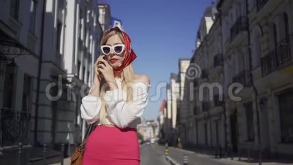 可爱的年轻女子站在街上用手机说话有魅力的时髦女孩在老房子里享受阳光视频的预览图