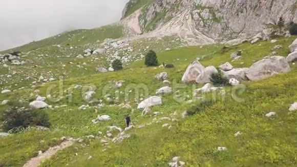 在绿色草地上的大石头间漫步在山路上的一位女医生视频的预览图