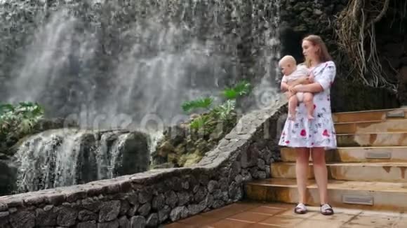 在一次家庭旅行中坐在母亲身边婴儿笑着看着瀑布视频的预览图