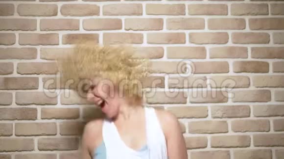 有趣的喜剧金发女孩与飘扬卷曲的短发砖墙背景复制空间情感观念快乐乐趣视频的预览图