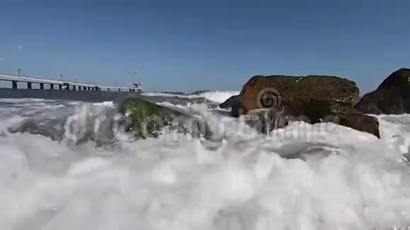 缓慢运动的海浪溅起水花在长满绿藻的石头上视频的预览图