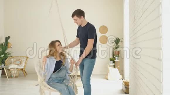 男人挥动现代悬挂柳条椅子亲吻坐着的女孩视频的预览图