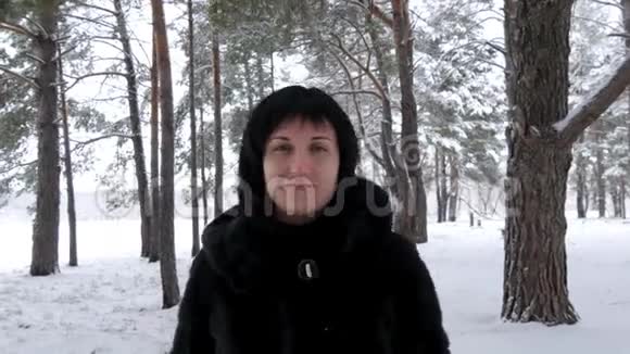 一个穿着黑色外套的年轻女人在寒冷的日子穿过一片雪林或公园看着镜头相机视频的预览图
