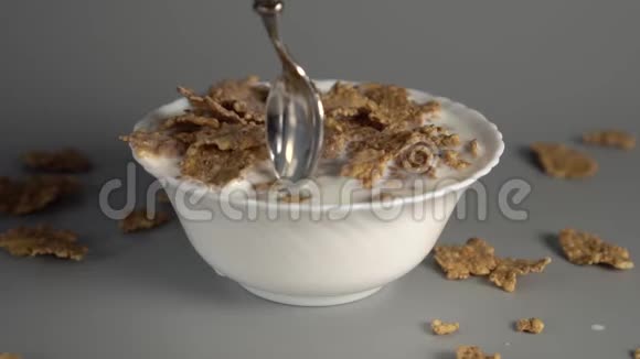 一个男人在灰色背景的白色盘子里搅拌一勺麦片粥和膳食牛奶视频的预览图