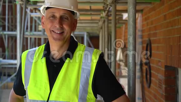 建筑工地上的男建筑工人站在脚手架上双臂交叉笑着对着镜头微笑视频的预览图