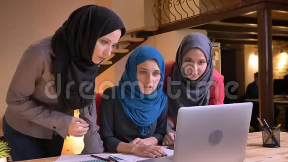三名阿拉伯女性办公室工作人员戴着头巾用手提电脑讨论数据的特写照片视频的预览图