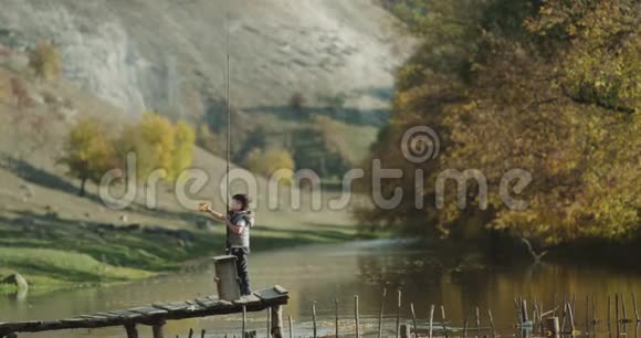 一个可爱的小男孩拿着一根大鱼竿在湖边的一座桥上玩视频的预览图