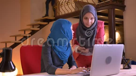 两位年轻漂亮的穆斯林女商人的特写肖像在笔记本电脑前有感情地讨论一个话题视频的预览图