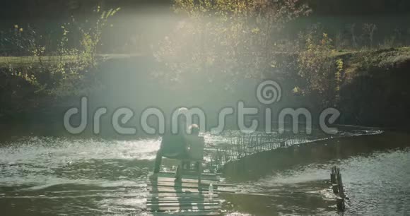 爸爸和他的儿子坐在桥顶上的椅子上从湖里钓鱼慢慢慢慢视频的预览图