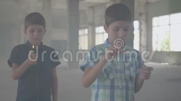 两个男孩在一个烟雾弥漫的废弃房间里一个男孩拿着燃烧的火柴第二个男孩拿着燃烧的打火机视频的预览图