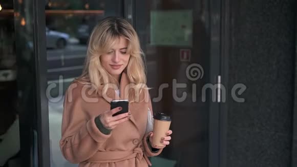 金发女人站在咖啡馆附近用她的智能手机视频的预览图