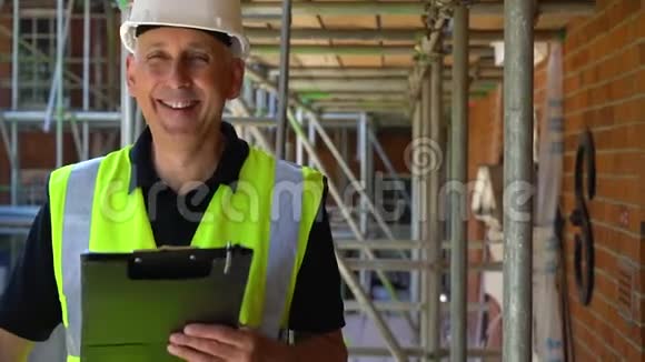 建筑工地上的男建筑工人站在脚手架上拿着剪贴板笑着对着镜头微笑视频的预览图