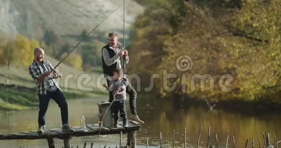 钓鱼时间为两个朋友和一个小男孩在晴天用钓鱼竿钓鱼4k视频的预览图