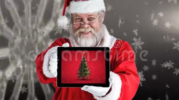 圣诞快乐的圣诞老人手里拿着一个数字平板电脑展示圣诞树视频的预览图